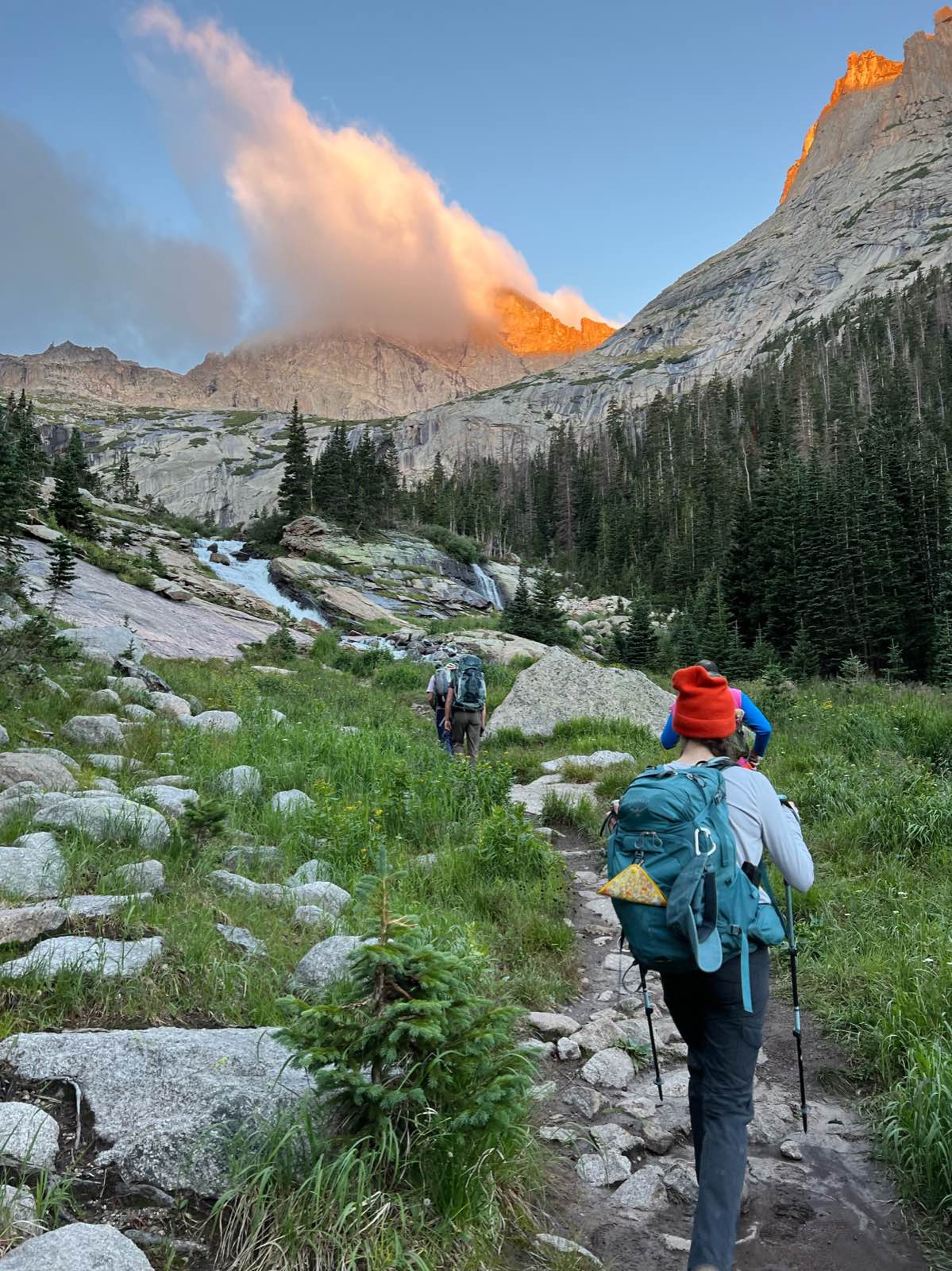 A hiker in a sun hoodie and backpack standing on a rocky summit ridge.