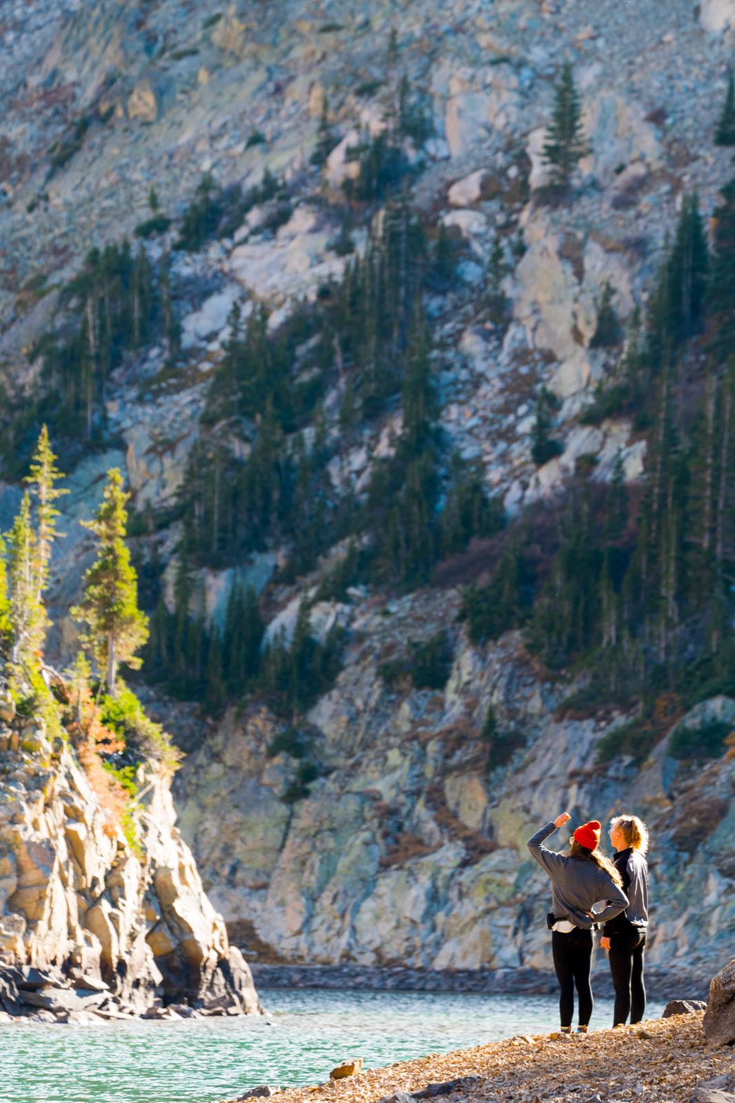 A hiker on a narrow rocky ridgeline above the treeline, mountains in the background.