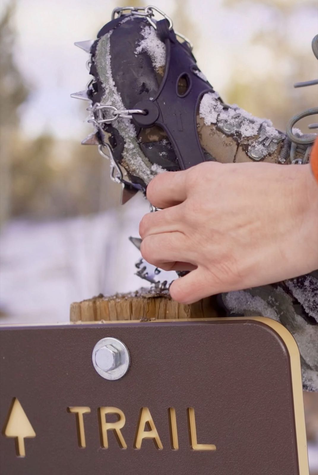 A pair of microspikes with metal traction studs resting on a snowy wooden trail sign.