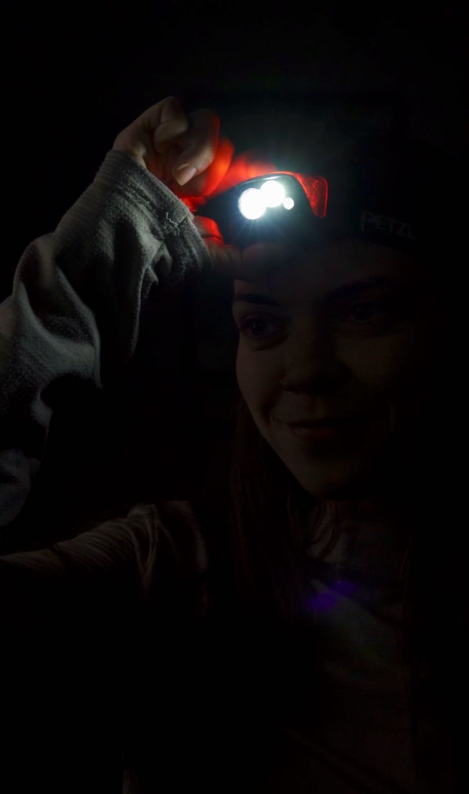 A hiker's headlamp glows in the dark as she adjusts it on her head.