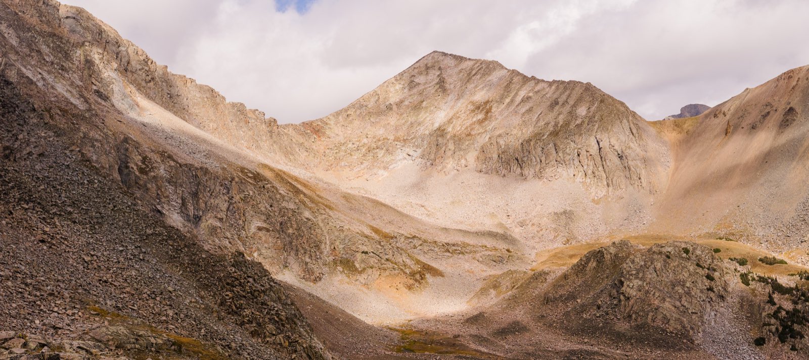 A pale, sunlit peak rises above a boulder-strewn basin dotted with pines.